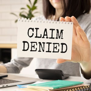 A woman holds a paper with 'Claim Denied' written on it, symbolizing a denied worker's compensation claim.